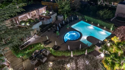 Beleuchteter Swimmingpool mit Whirlpool in einem Garten bei Nacht