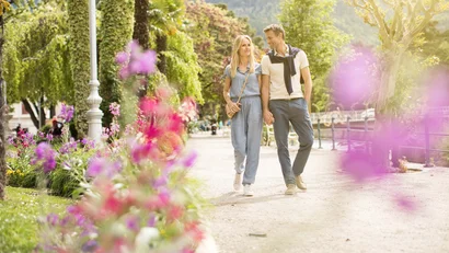 Paar hält Händchen und spaziert an blühenden Büschen in sonnigem Park