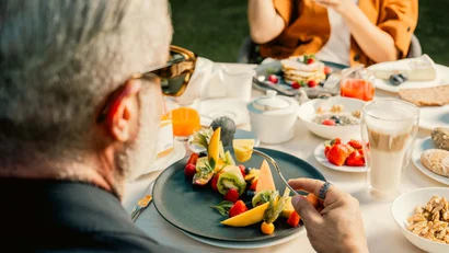 Person isst Obstsalat bei einem gedeckten Frühstückstisch im Freien