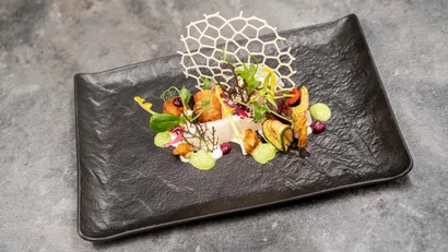 Kunstvoll angerichtetes Gourmetgericht auf rechteckigem schwarzem Teller