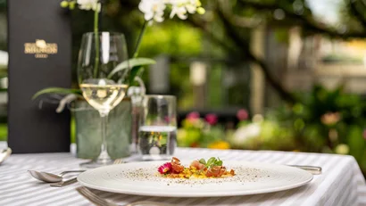 Fein angerichtetes Gourmetgericht mit Weißwein auf gedecktem Tisch im Garten