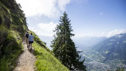 Wanderer auf Bergpfad mit Blick ins Tal und bewölktem Himmel