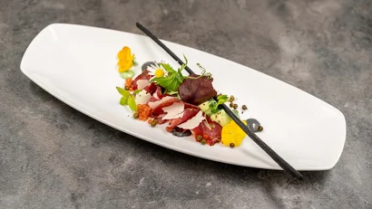 Gourmetgericht mit Fleisch, Blüten, Kräutern und Dekoration auf weißem Teller