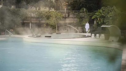 Thermalpool mit dampfendem Wasser und Person im Bademantel am Rand