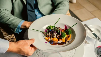 Ein Kellner serviert ein kunstvoll angerichtetes Gericht mit Gemüse und Soße.