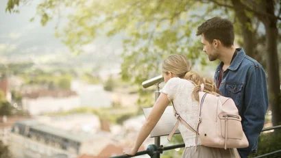 Junges Paar schaut durch ein Fernglas auf eine Stadtansicht im Freien
