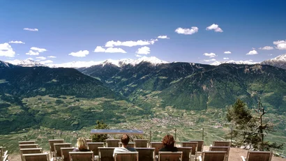 Menschen sitzen auf Stühlen mit Blick auf Berge und Tal