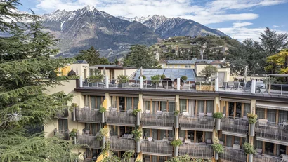 Hotel mit Balkonen vor schneebedeckten Bergen und bewölktem Himmel