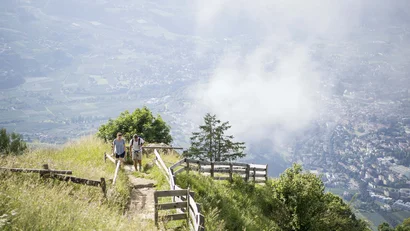 Zwei Wanderer auf Bergweg mit Blick auf Tal und Wolken