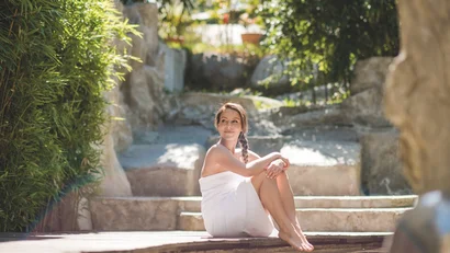 Frau im weißen Handtuch sitzt entspannt am Wasser im Außenbereich