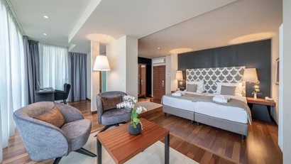 Modern eingerichtetes Hotelzimmer mit zwei Sesseln, Bett und Schreibtisch