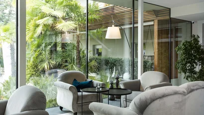 Gemütliche Sitzecke mit grauen Sesseln vor großen Glasfenstern und grünen Pflanzen