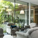 Gemütliche Sitzecke mit grauen Sesseln vor großen Glasfenstern und grünen Pflanzen