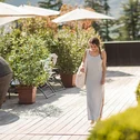 Woman in striped maxi dress walking on sunny terrace with plants