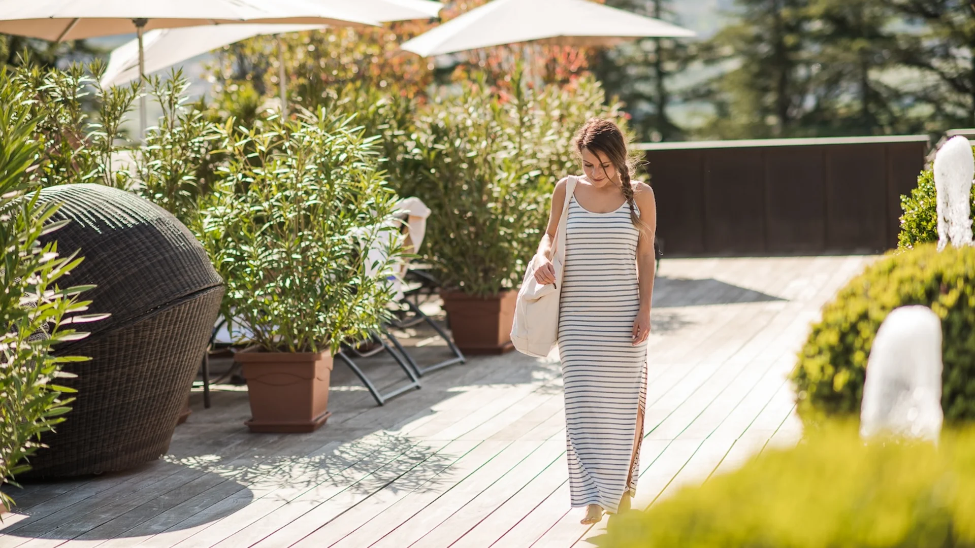 Woman in striped maxi dress walking on sunny terrace with plants