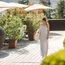 Woman in striped maxi dress walking on sunny terrace with plants