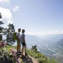 Zwei Wanderer genießen den Ausblick von einem Berg auf ein Tal und eine Stadt