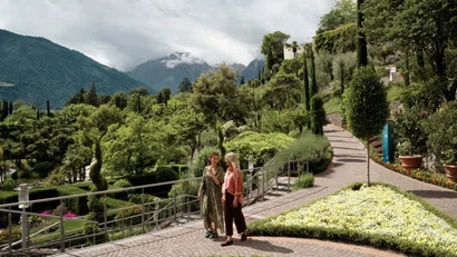 Zwei Frauen spazieren in einem blühenden Berggarten bei bewölktem Himmel