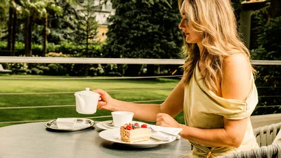 Frau sitzt draußen und gießt Tee mit Kuchen auf dem Tisch